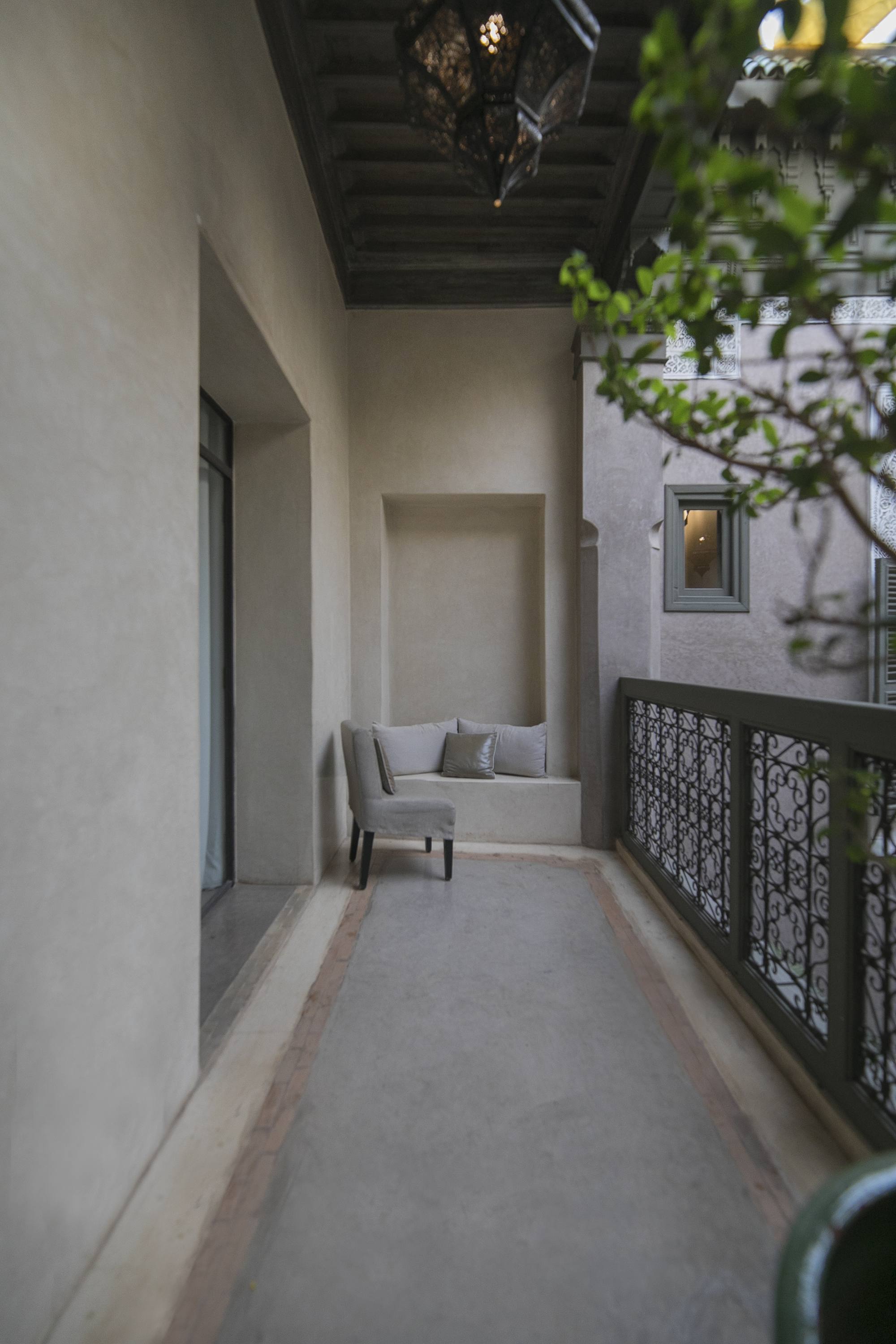 La coursive à l'étage du Riad Dar One — banquette et fauteuil dans l'alcôve, grande lanterne ajourée, ferronneries sur le patio et une fenêtre éclairée en face