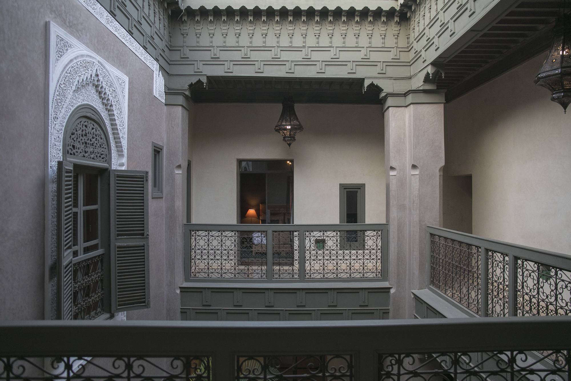 La galerie du patio au Riad Dar One — lanternes suspendues au bois sculpté, une lampe déjà allumée dans une chambre ouverte