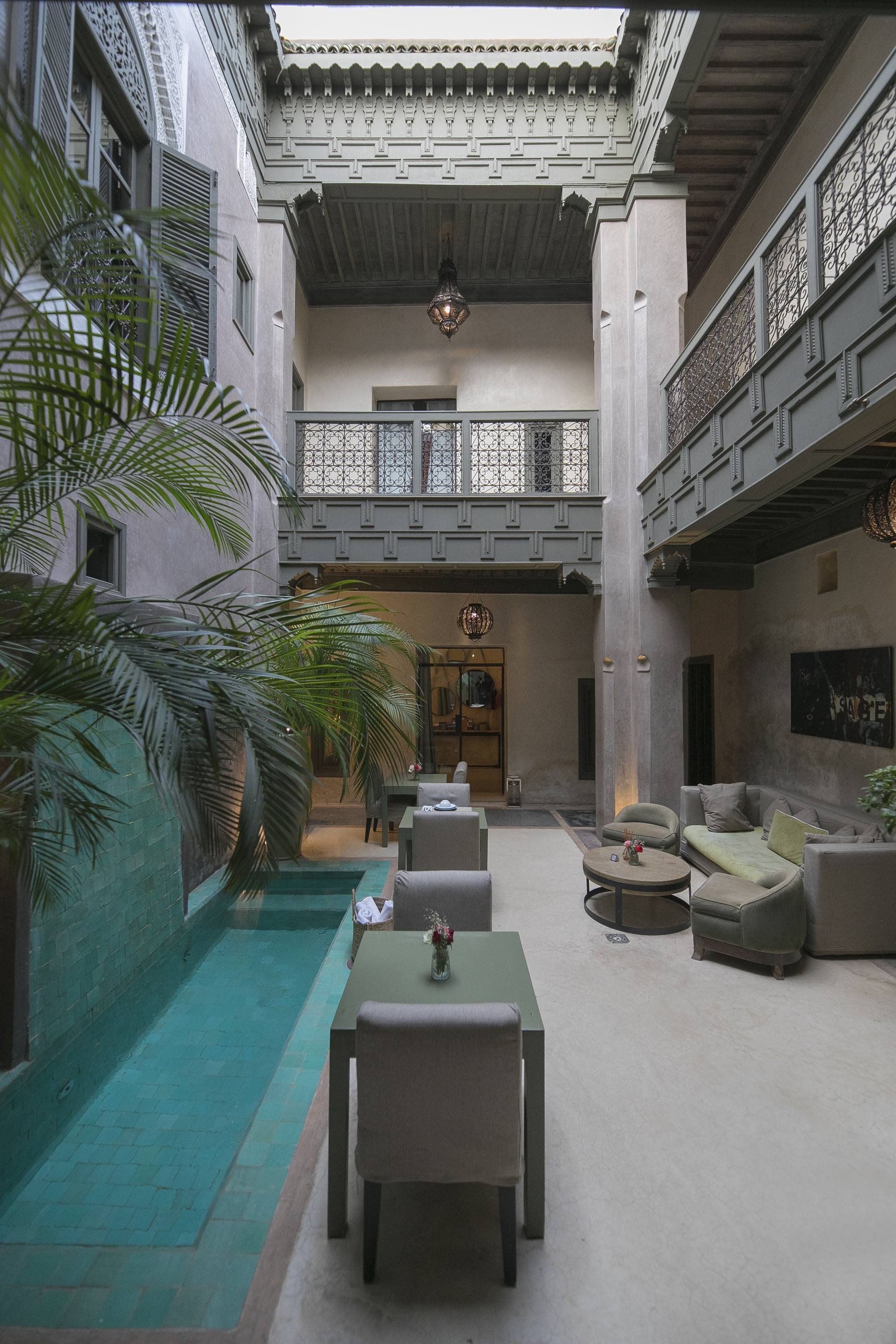 Le patio du Riad Dar One — la piscine de zellige vert d’eau au pied du grand palmier, les banquettes du salon d’été au fond