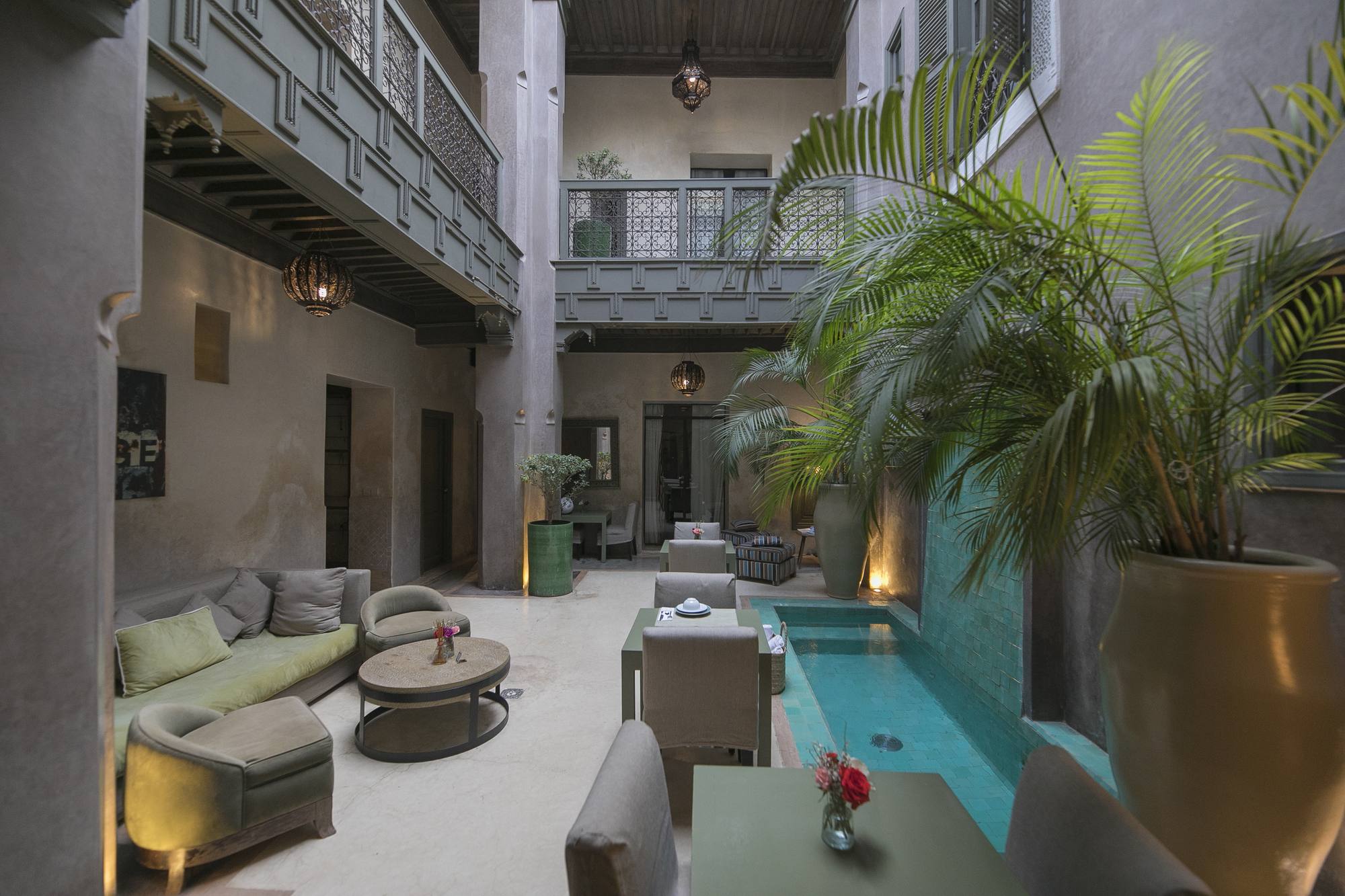 Le patio côté salon d’été — canapés profonds autour de la table basse, la piscine et les tables dressées en vis-à-vis