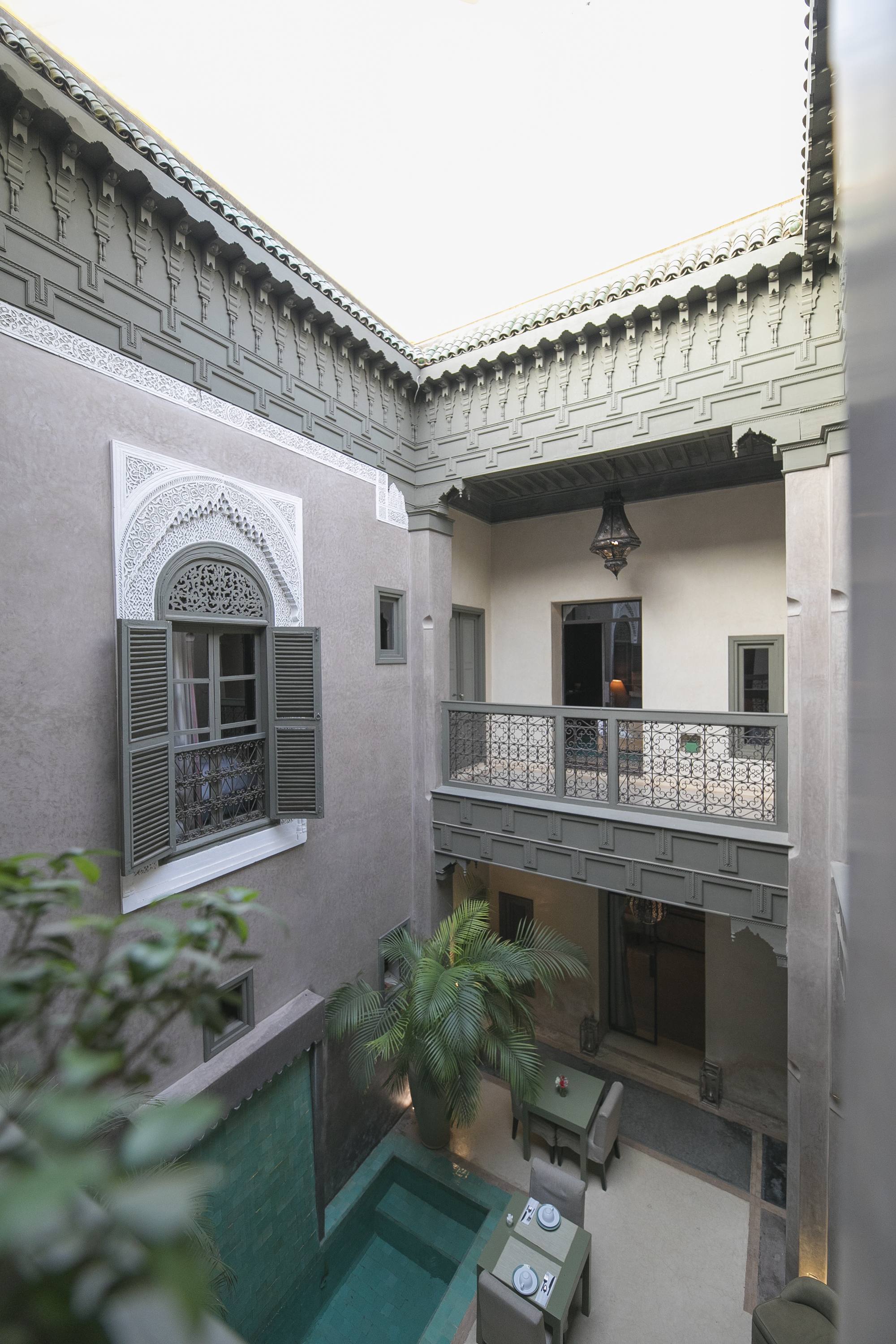 Le patio du Riad Dar One vu d’en haut — la piscine, le grand palmier et le salon d’été sous la galerie