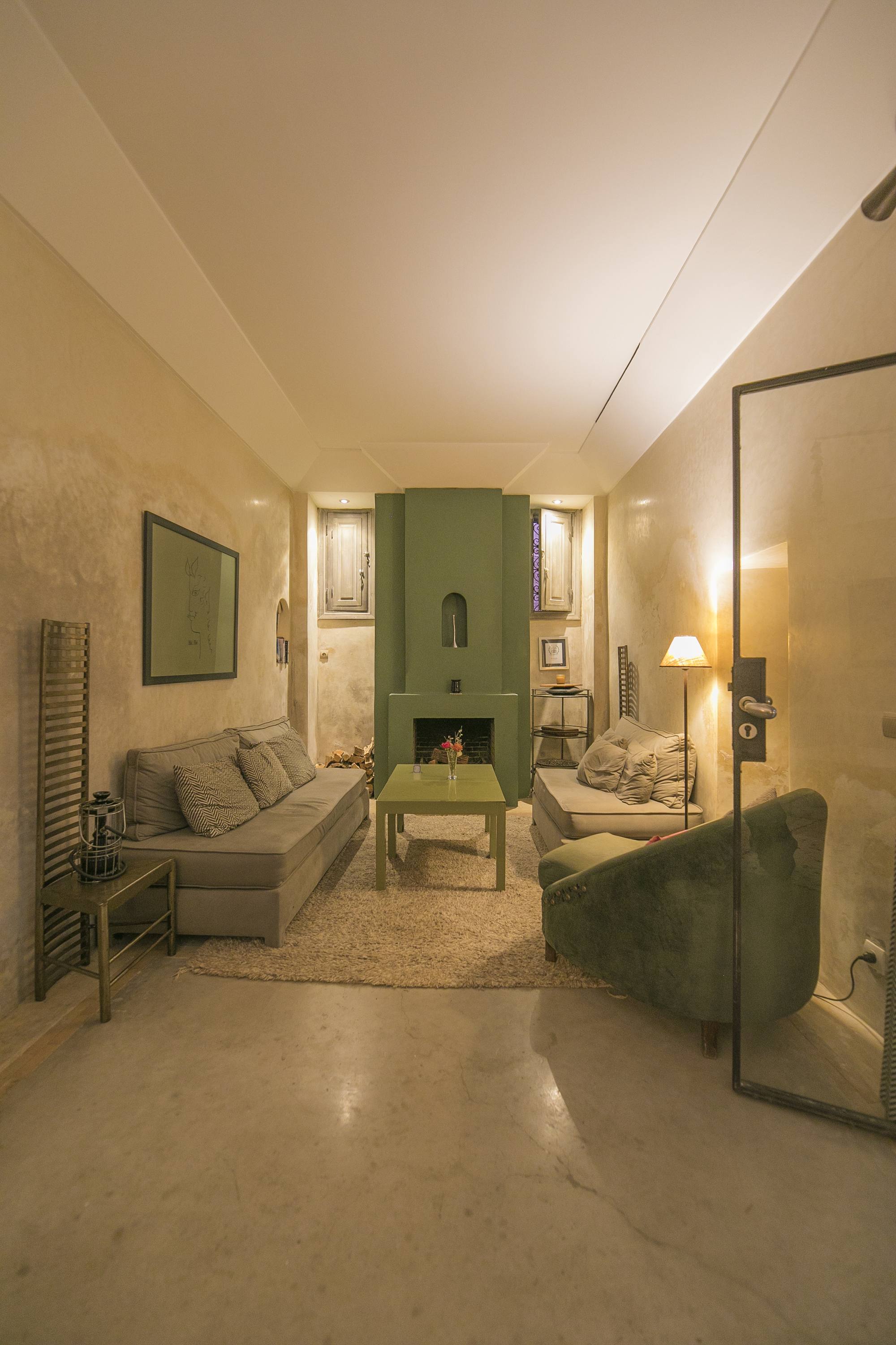 Le salon à cheminée de Dar One — canapés autour de la table basse, un dessin encadré au mur, le bois prêt pour la flambée