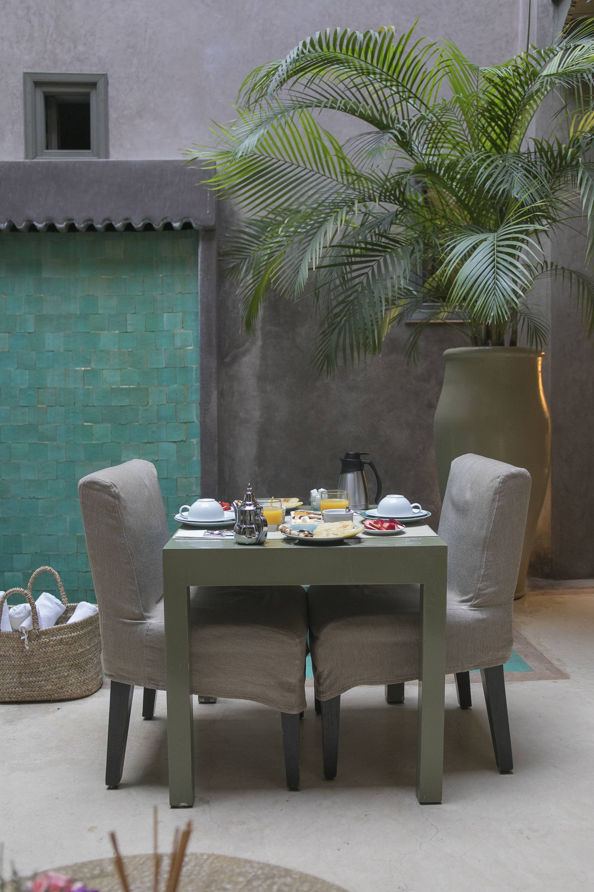 La table pour deux dressée dans le patio du Riad Dar One — théière d'argent, mur de zellige vert et grand palmier en pot