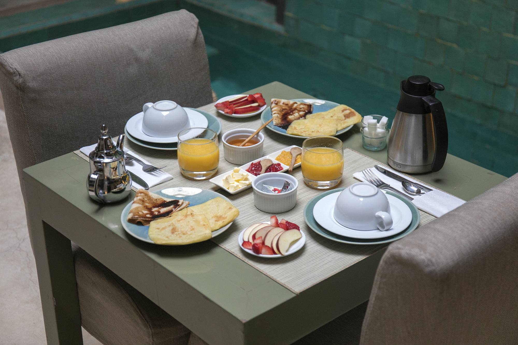 Le petit-déjeuner pour deux dressé au bord de la piscine — crêpes et msemen, jus d'orange pressé, théière d'argent et fruits frais